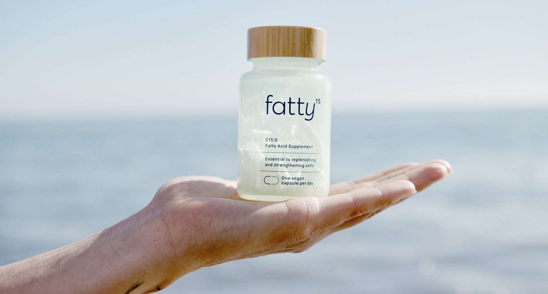 Hand holding Fatty15's C15 supplement bottle by the beach.