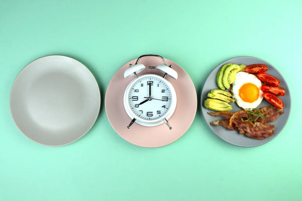 Empty plate, clock, breakfast with avocado, egg, and bacon on green background.