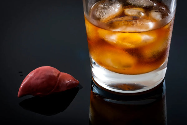 Glass of whiskey with ice next to a liver model on a black surface.