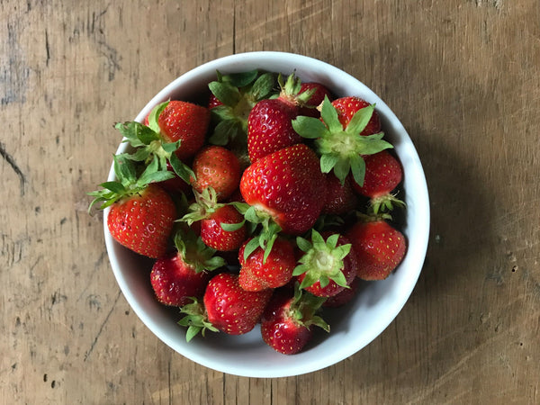 Bowl of fresh strawberries on wooden table.