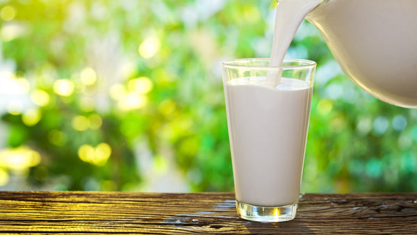 Pouring fresh milk into glass on wooden table outdoors.