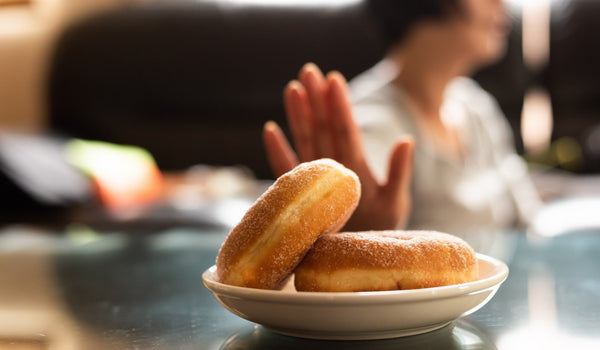 Person rejecting plate of glazed donuts on the table.
