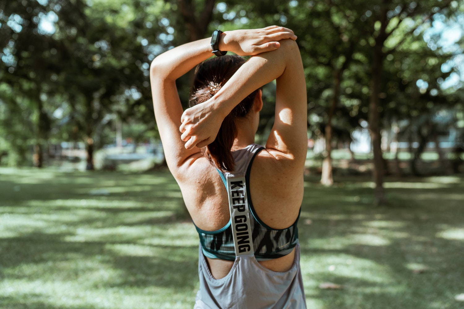 Woman stretching arms in park with motivational tank top.