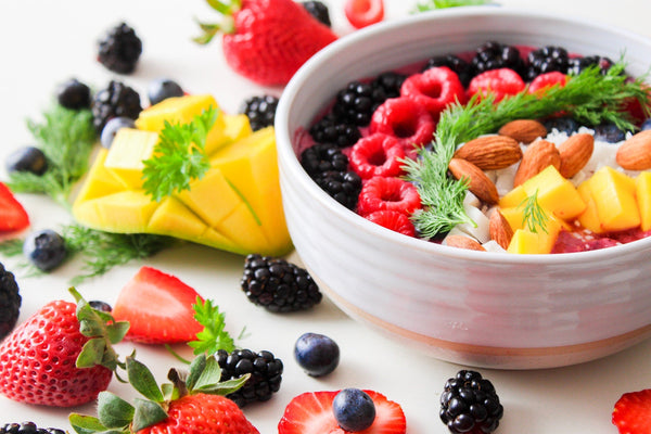 Bowl of mixed berries, mango, and almonds with fresh herbs.
