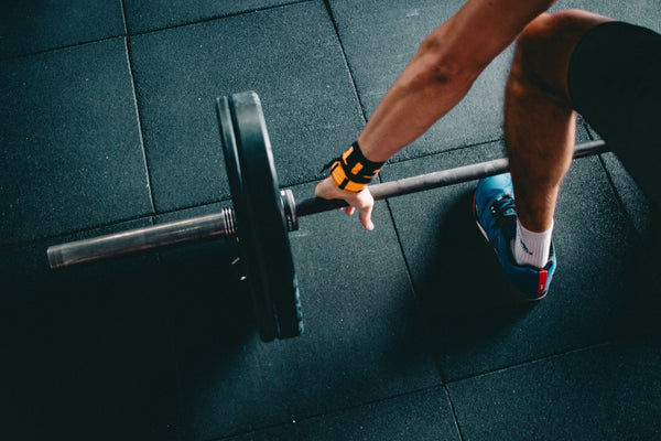 Person lifting barbell in a gym with weightlifting wrist strap.