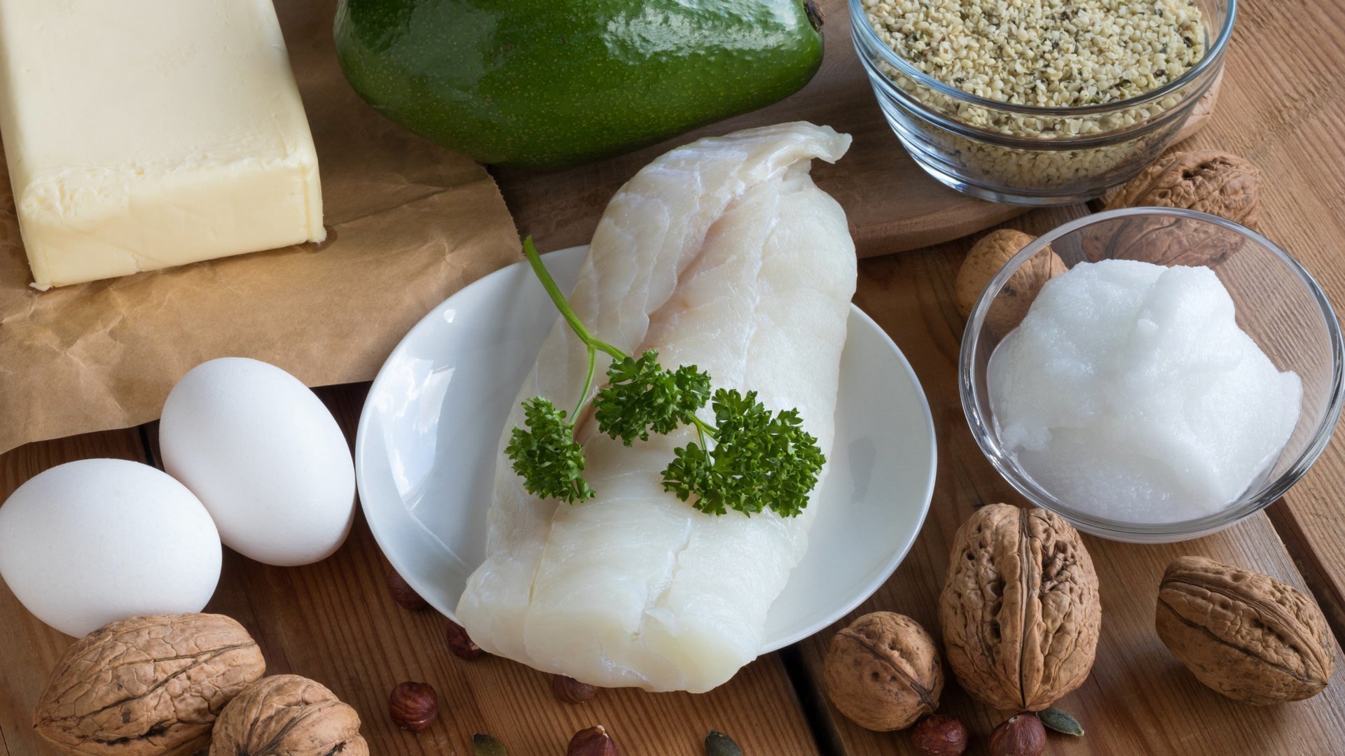 Healthy fats and protein sources including eggs, fish, and nuts on a wooden table.