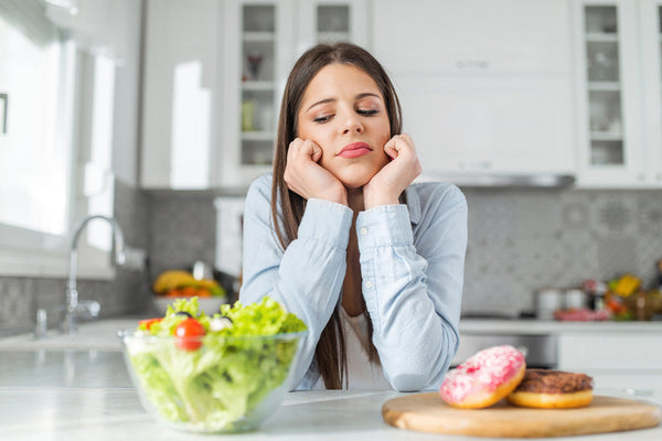 Woman deciding between salad and donuts in kitchen.