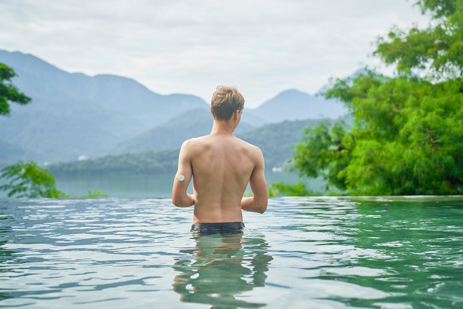 Man in infinity pool overlooking mountains and trees.