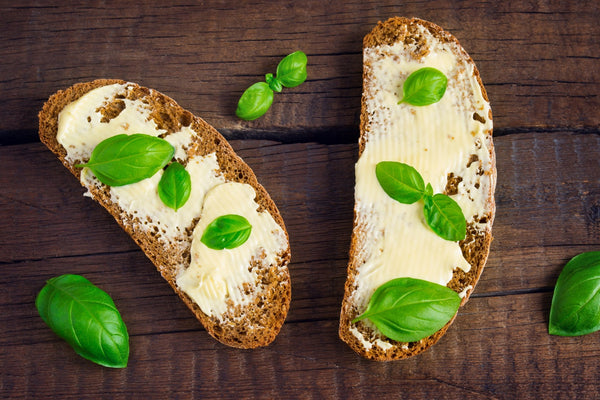Whole grain bread with butter and fresh basil leaves on wooden table.