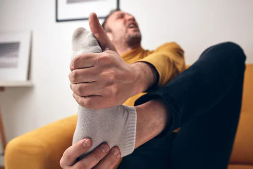 Man holding sore foot, sitting on yellow couch in living room.