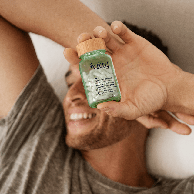 
                Man smiling while holding Fatty15&#39;s C15 supplement in bed.