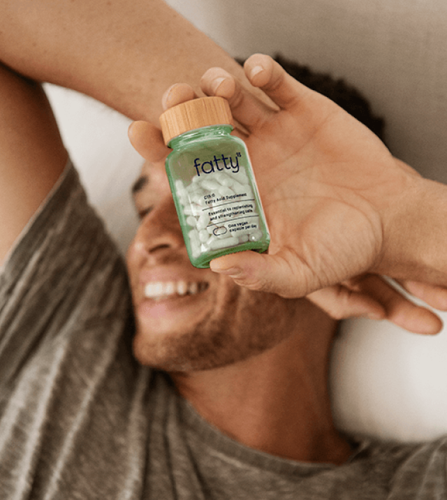 Man smiling in bed holding Fatty15's C15 supplement bottle.